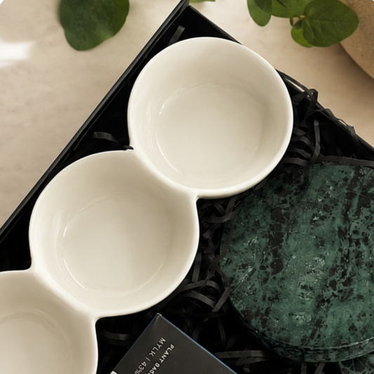 Two white ceramic spoons on a black tray with green leaves in the background