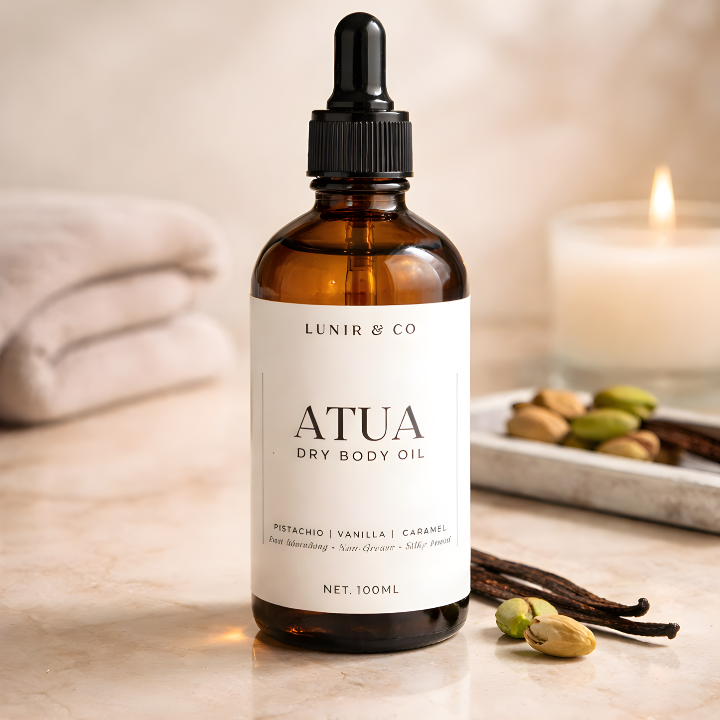 Bottle of ATUA dry body oil by Lunir & Co on a wooden surface with vanilla beans and a candle in the background.