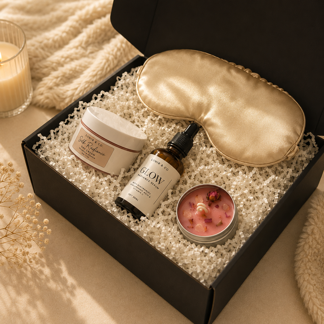 Gift set with skincare products, eye mask, and candle in a box on a soft surface.