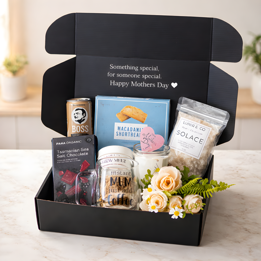 Gift box with various items including a can of Boss, a jar of Solace, and flowers on a light background.