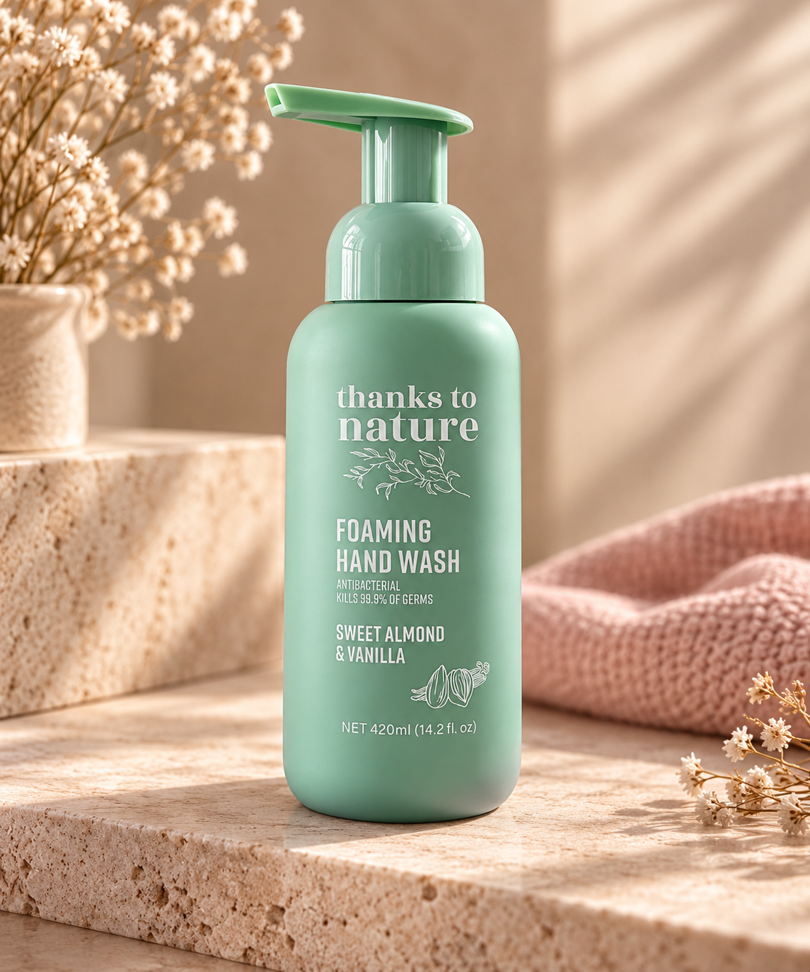 A mint green pump bottle of 'thanks to nature' Foaming Hand Wash, styled on a stone surface with dried flowers and a pink knit blanket in the background.
