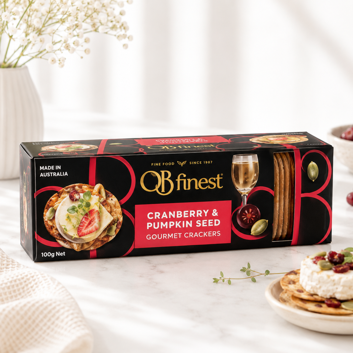 Box of OB Finest cranberry and pumpkin seed gourmet crackers on a table with a plate of crackers and a glass of wine.