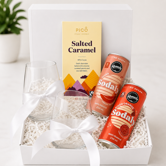 Gift set with a glass, two cans of soda, and a box of salted caramel on a white background.