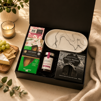 Gourmet gift box with snacks and a marble-patterned plate on a decorative table.