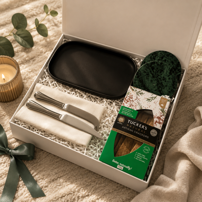 Gift set with black tray, knives, and crackers in a box on a soft surface.