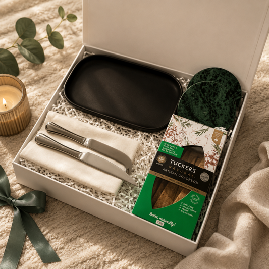 Gift set with black tray, knives, and crackers in a box on a soft surface.