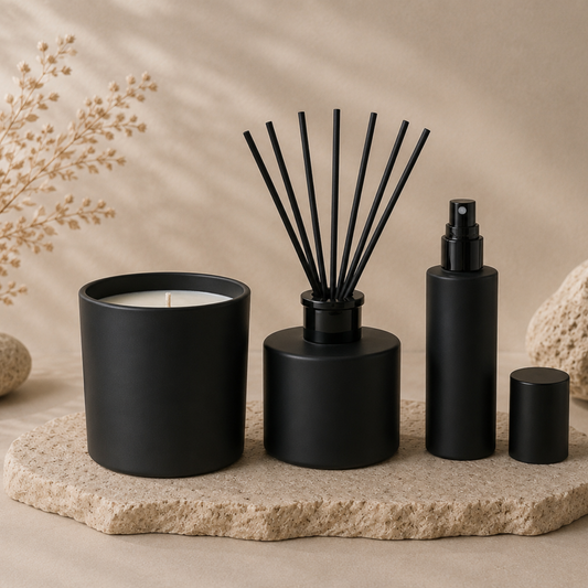 Set of black home fragrance items including a candle, diffuser, and bottles on a stone surface with a neutral background.