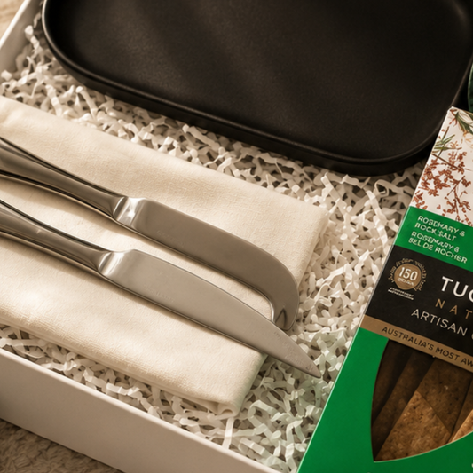 Set of silver cutlery with a black tray and Tucci chocolate packaging on a textured surface.