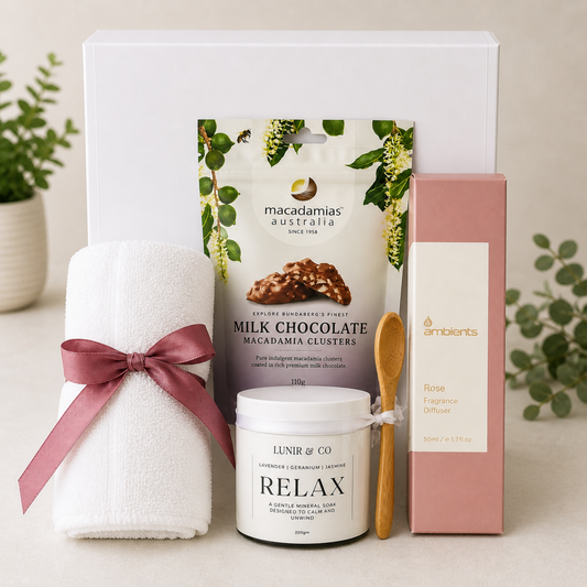Gift set with a towel, chocolate clusters, candle, and diffuser on a neutral background.
