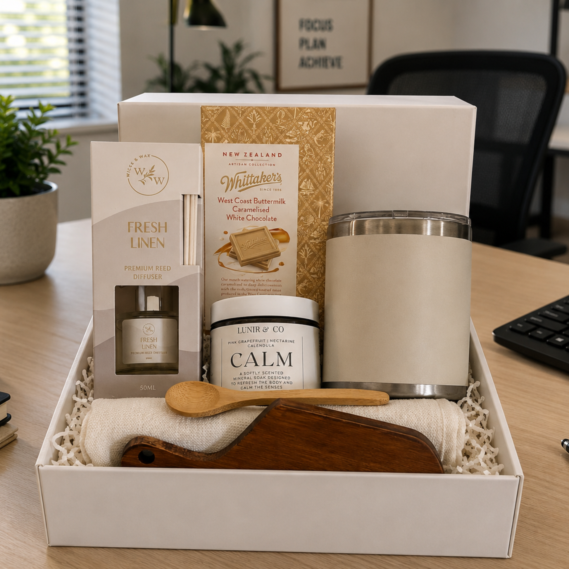 Gift box with various items including a candle, diffuser, and wooden spoon on a desk.