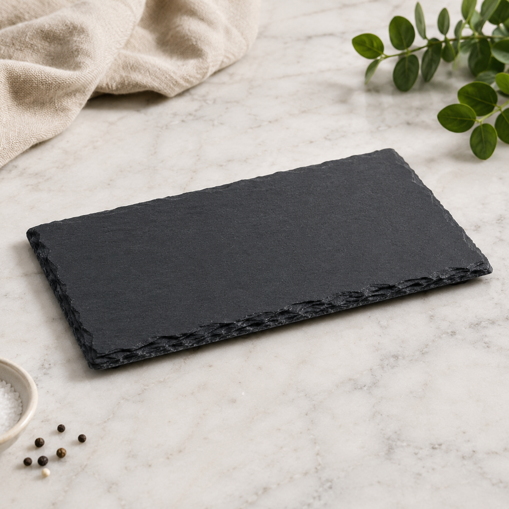 Black slate tray on a light gray surface with a beige towel and green leaves in the background.