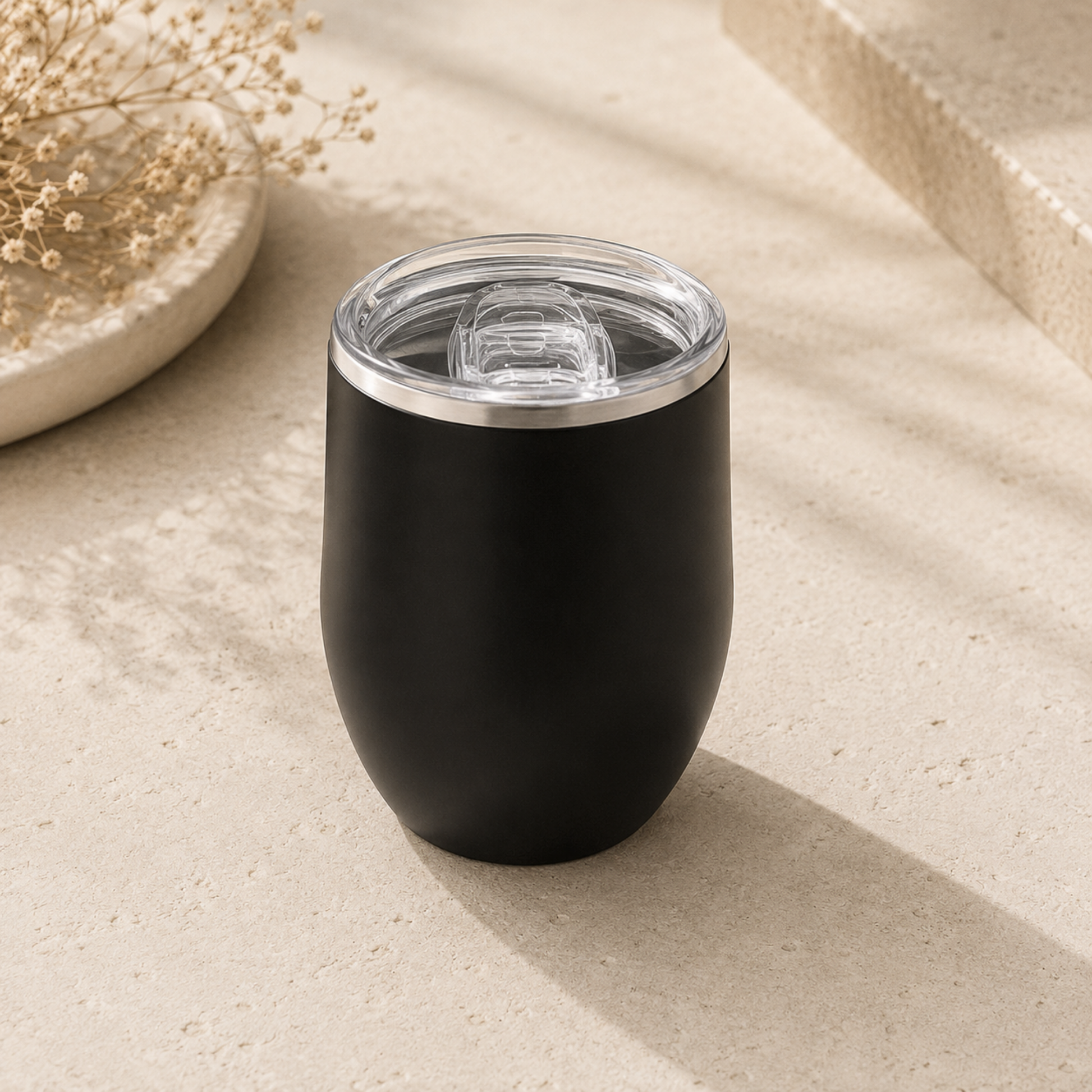 Black insulated tumbler with clear lid on a beige surface