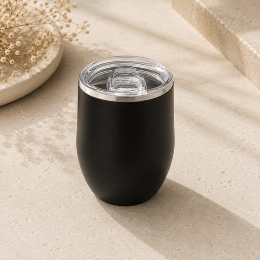 Black insulated tumbler with clear lid on a beige surface
