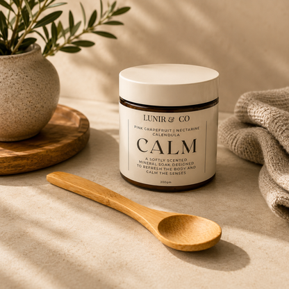 Jar of 'Calm' soap by Lunir & Co on a neutral background with a wooden spoon and plant.