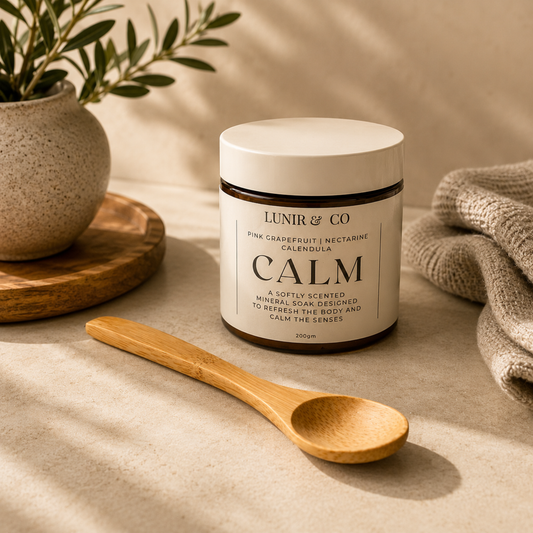 Jar of 'Calm' soap by Lunir & Co on a neutral background with a wooden spoon and plant.