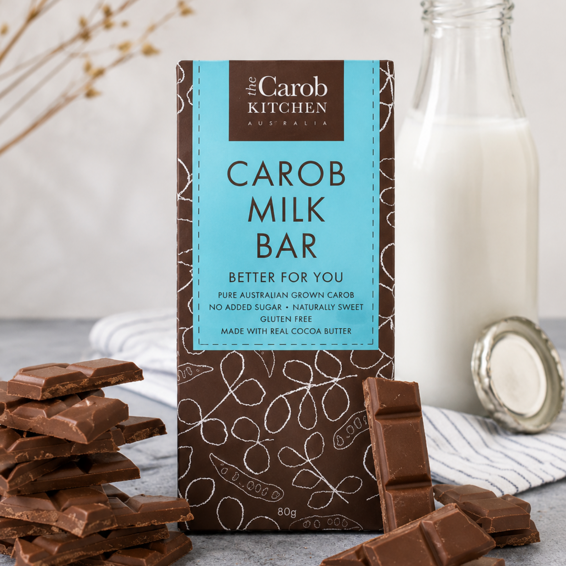 Carob milk bar packaging with carob bars and a bottle of milk on a light background