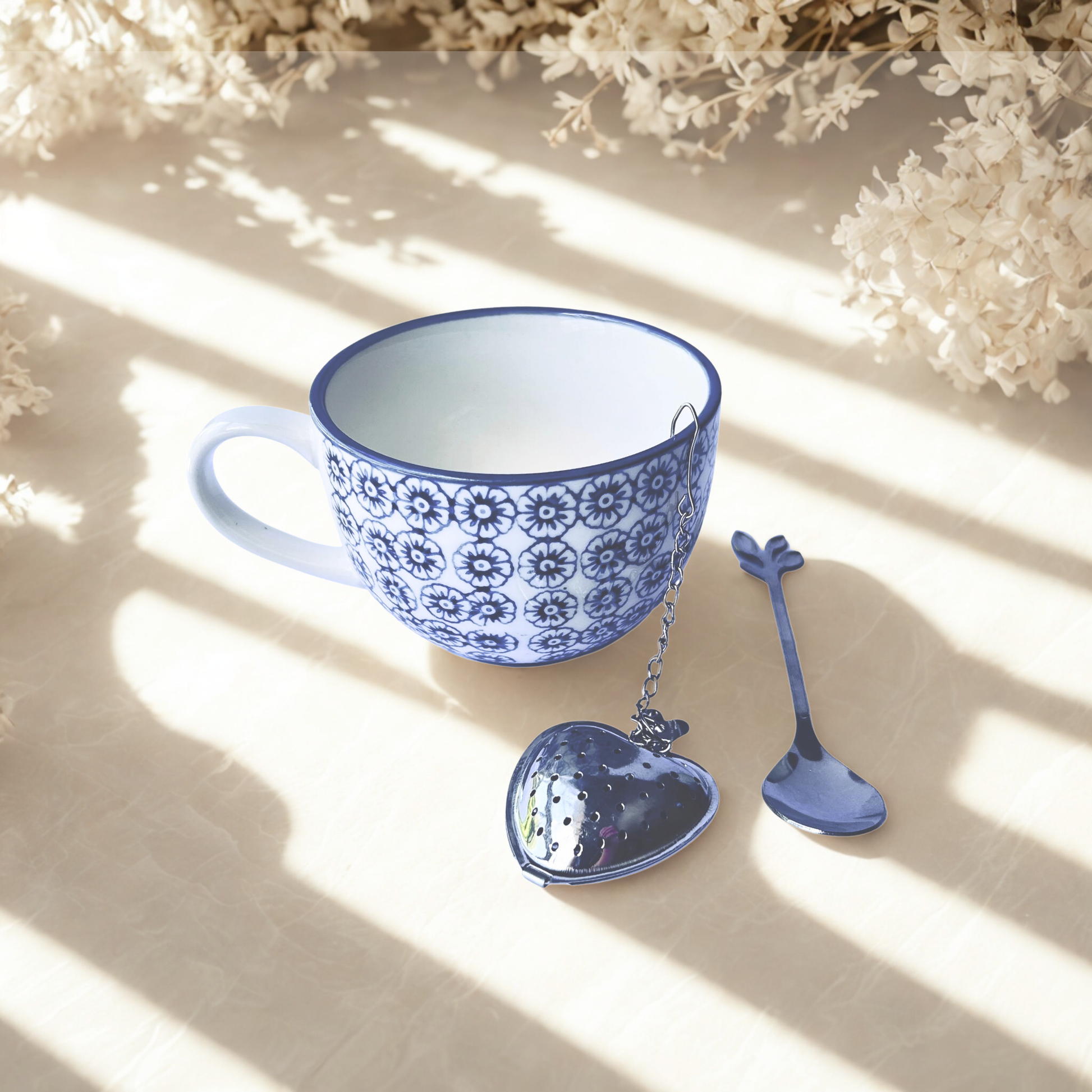 Blue and white ceramic tea cup with heart-shaped tea infuser and spoon on a light background