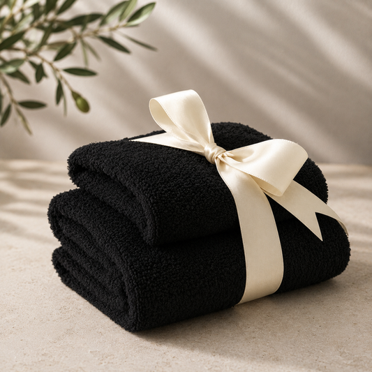 Two black folded towels tied with a white ribbon on a beige surface with a plant in the background.