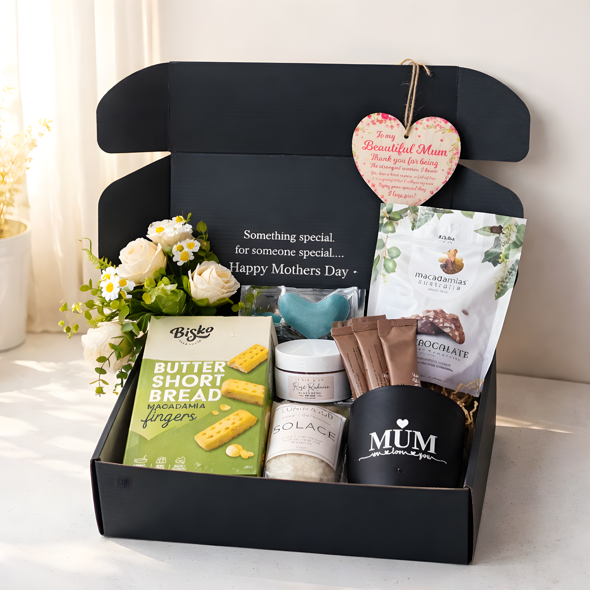 Gift box with Mother's Day items including a mug, cookies, and flowers on a light surface.