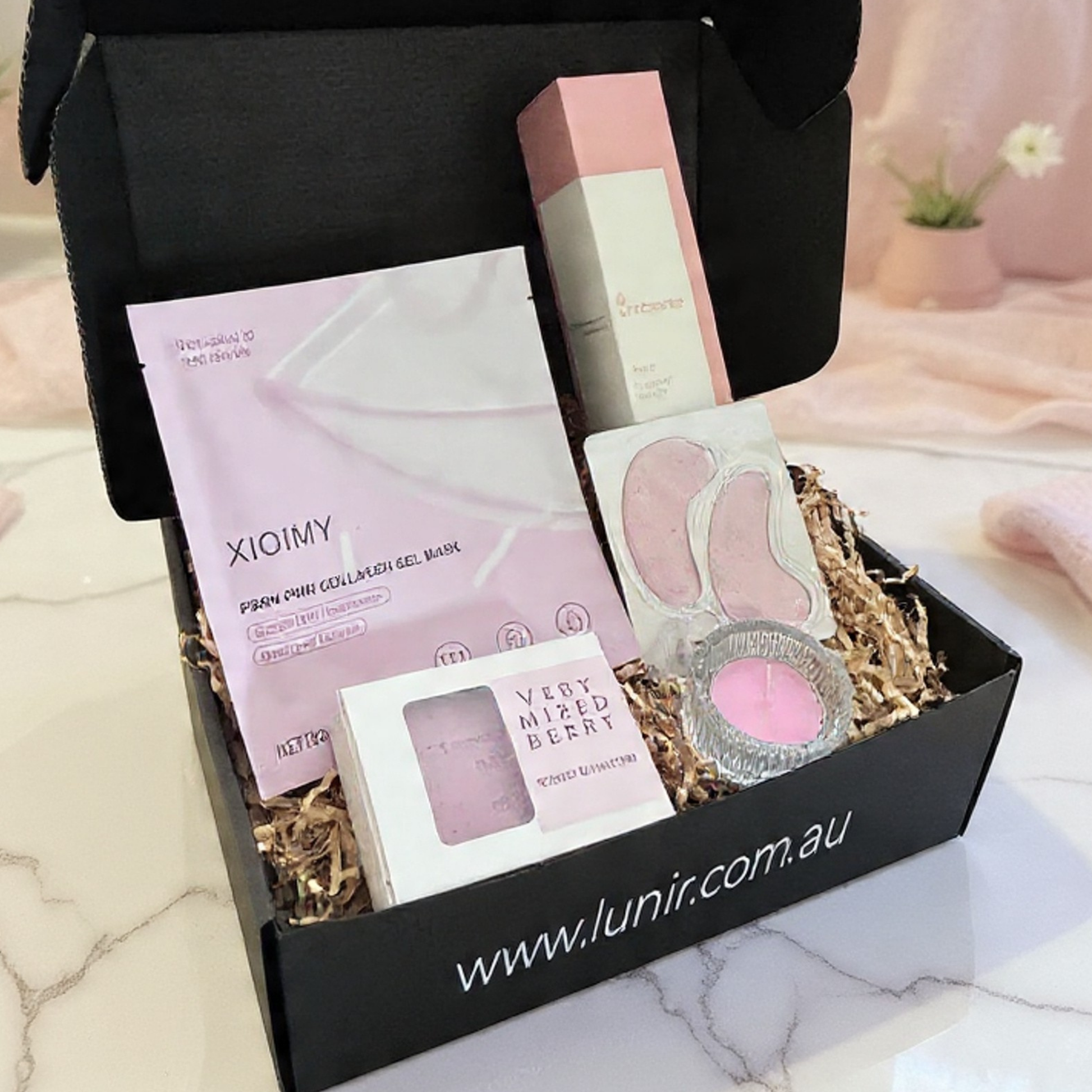 Black gift box with skincare products including a pink packet labeled 'Xiaomi' on a marble surface.