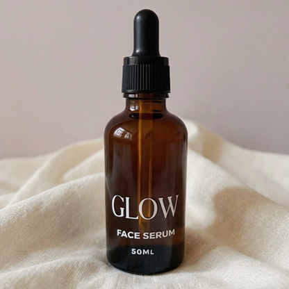 Brown glass bottle of face serum labeled 'GLOW' on a beige fabric background