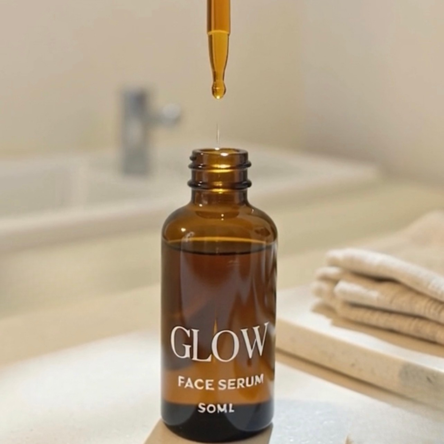 Brown bottle of 'GLOW' face serum with dropper on a bathroom counter.