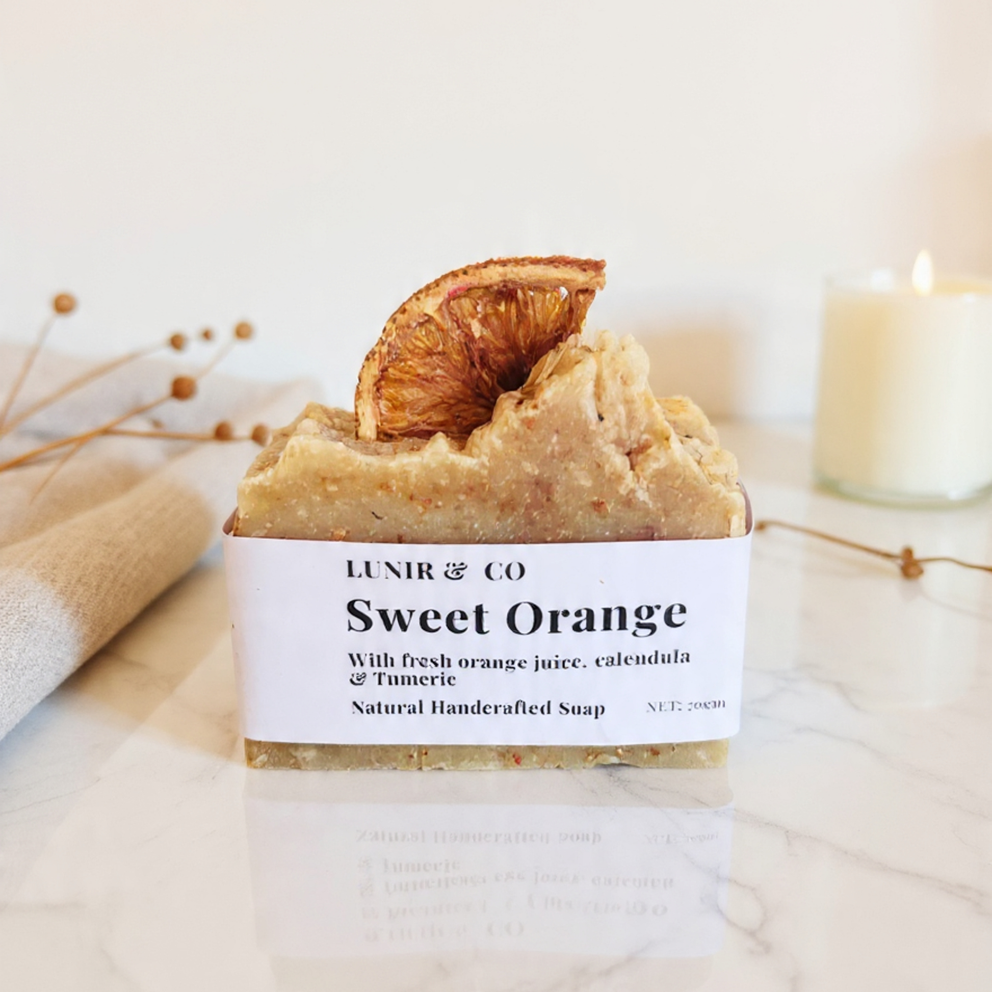 Bar of soap with a label reading 'Sweet Orange' from LUNIR & CO, garnished with a dried orange slice on a neutral background.