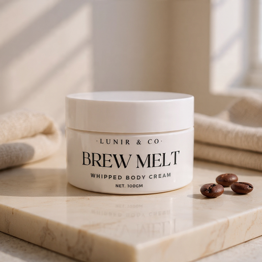Jar of 'Brew Melt' whipped body cream by Lunir & Co on a marble surface with coffee beans.