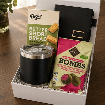 Gift box with black tumbler, Bisko Butter Shortbread, and Hugos Nibbles Bombs on a wooden surface.