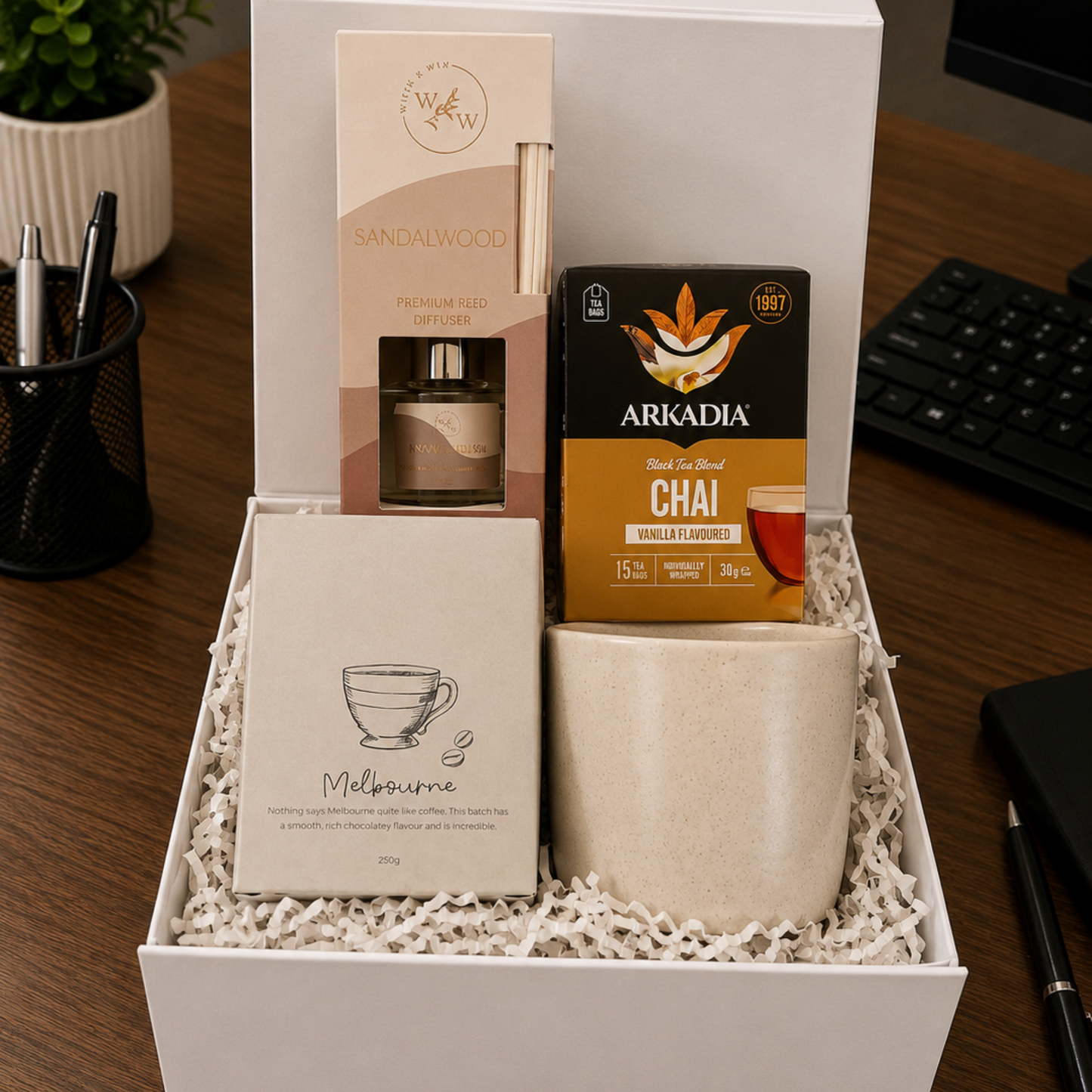 Gift box with a mug, tea packaging, and other items on a desk.