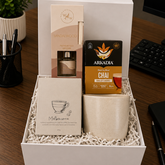Gift box with a mug, tea packaging, and other items on a desk.