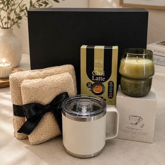 Gift set with folded towels, a mug, a box of Chai Latte, and a candle on a neutral background.