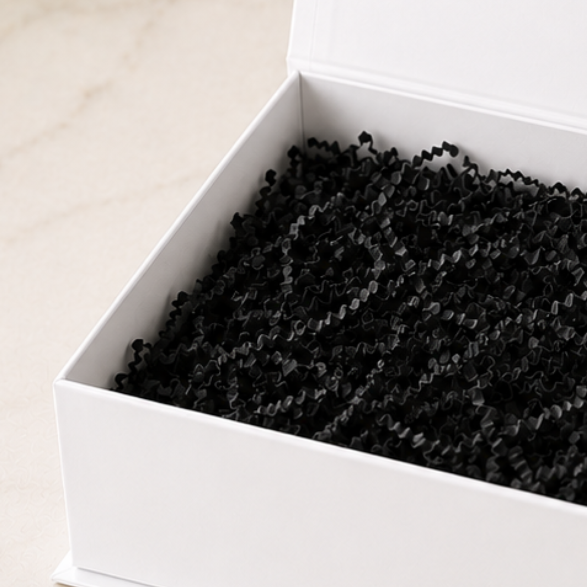 White box with black crinkle paper inside on a light beige background