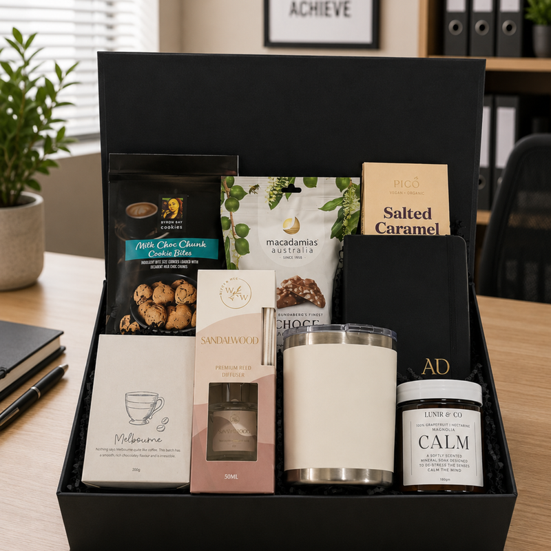 Gift basket with snacks, candles, and other items on a desk.