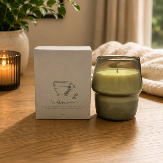 Candle in a glass holder with a box labeled 'Melbourne' on a wooden surface.