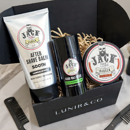 Men's grooming products including an after-shave balm, deodorant stick, and pomade in a branded box on a marble surface.