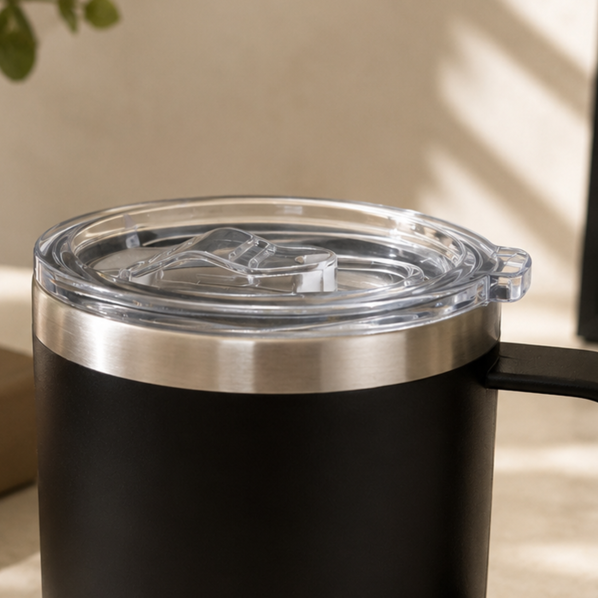 Black insulated tumbler with a clear lid on a light wooden surface.