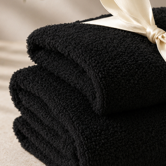 Stack of black towels with a beige ribbon on a neutral background