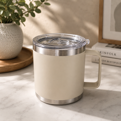 Beige mug with a clear lid on a marble surface, with a plant and books in the background.