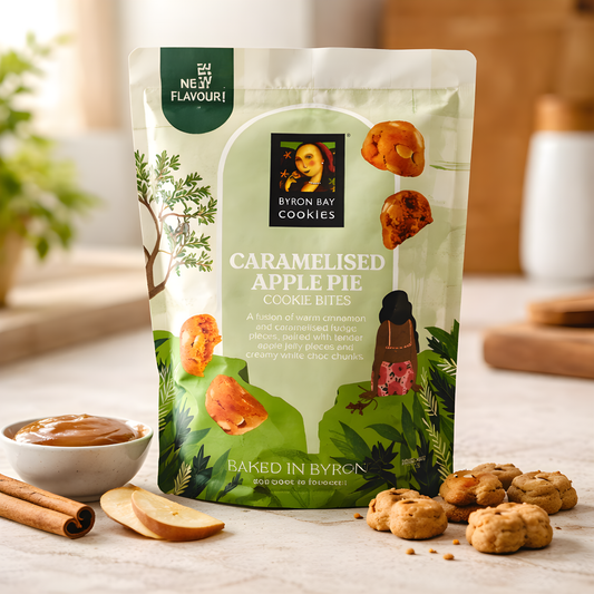 Packaging of Byron Bay Cookies Caramelised Apple Pie cookie bites on a table with cookies and ingredients.