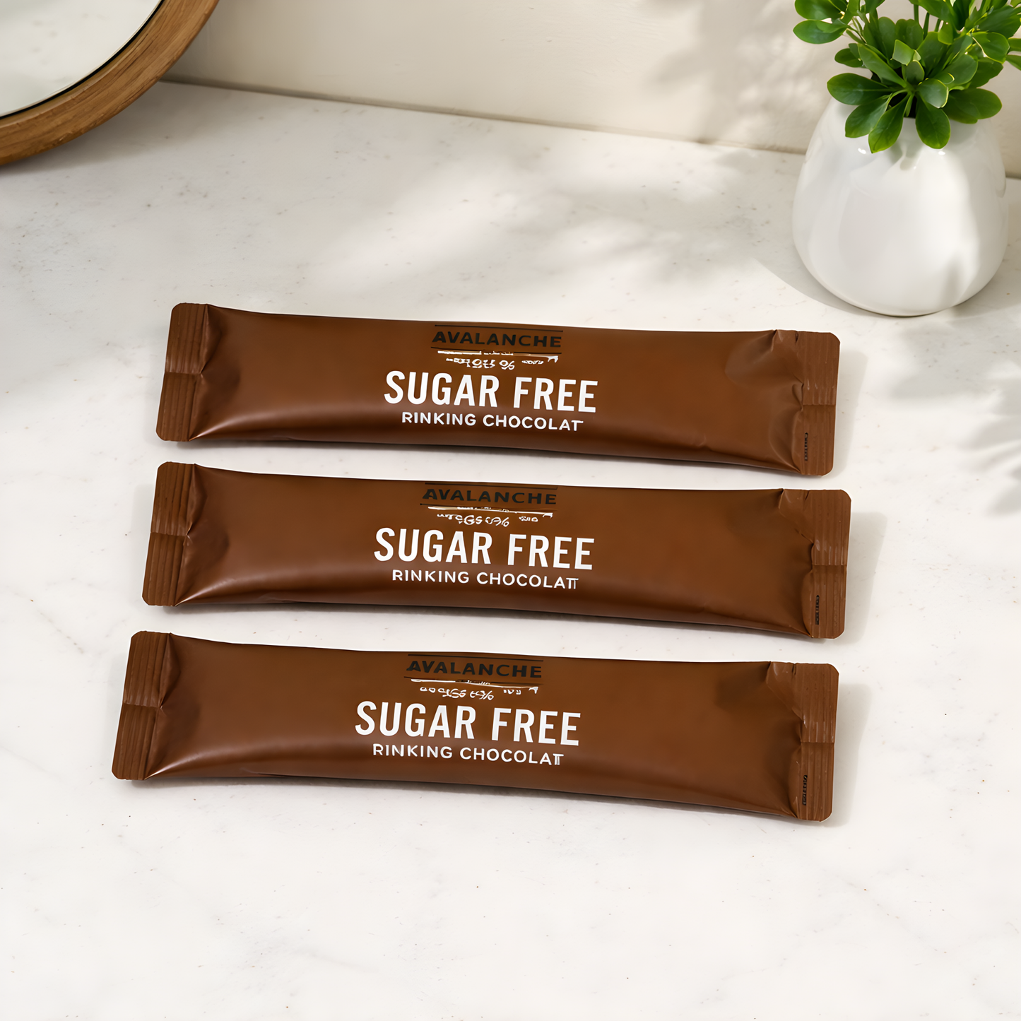 Three sugar-free chocolate bars from Avalanche on a white surface with a plant in the background.