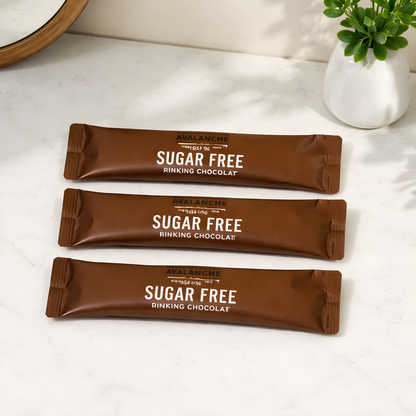 Three sugar-free chocolate bars from Avalanche on a white surface with a plant in the background.
