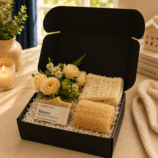 Gift set with sponges, flowers, and a candle in a black box on a table.