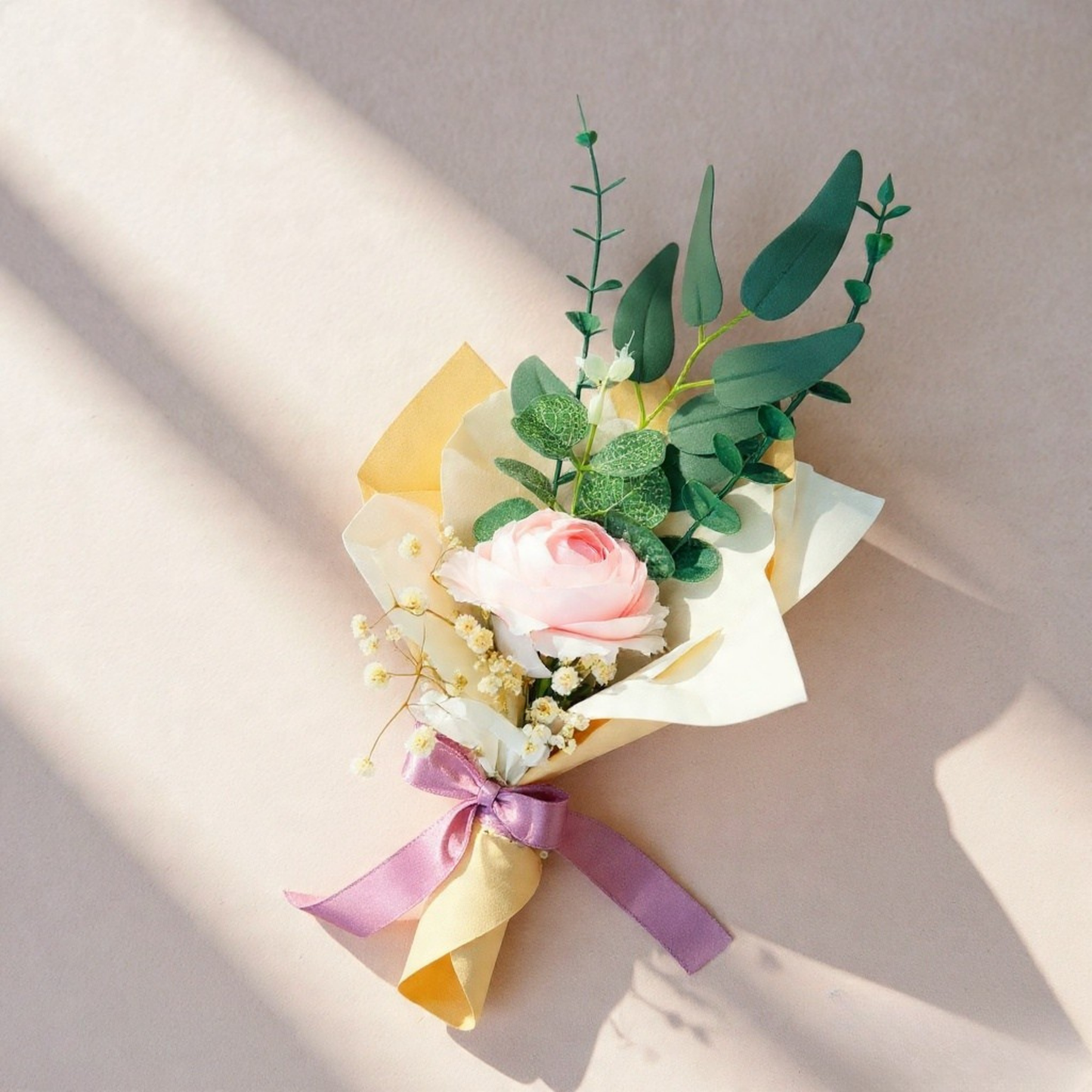 Bouquet of flowers with a pink rose and green leaves, tied with a purple ribbon on a light background.