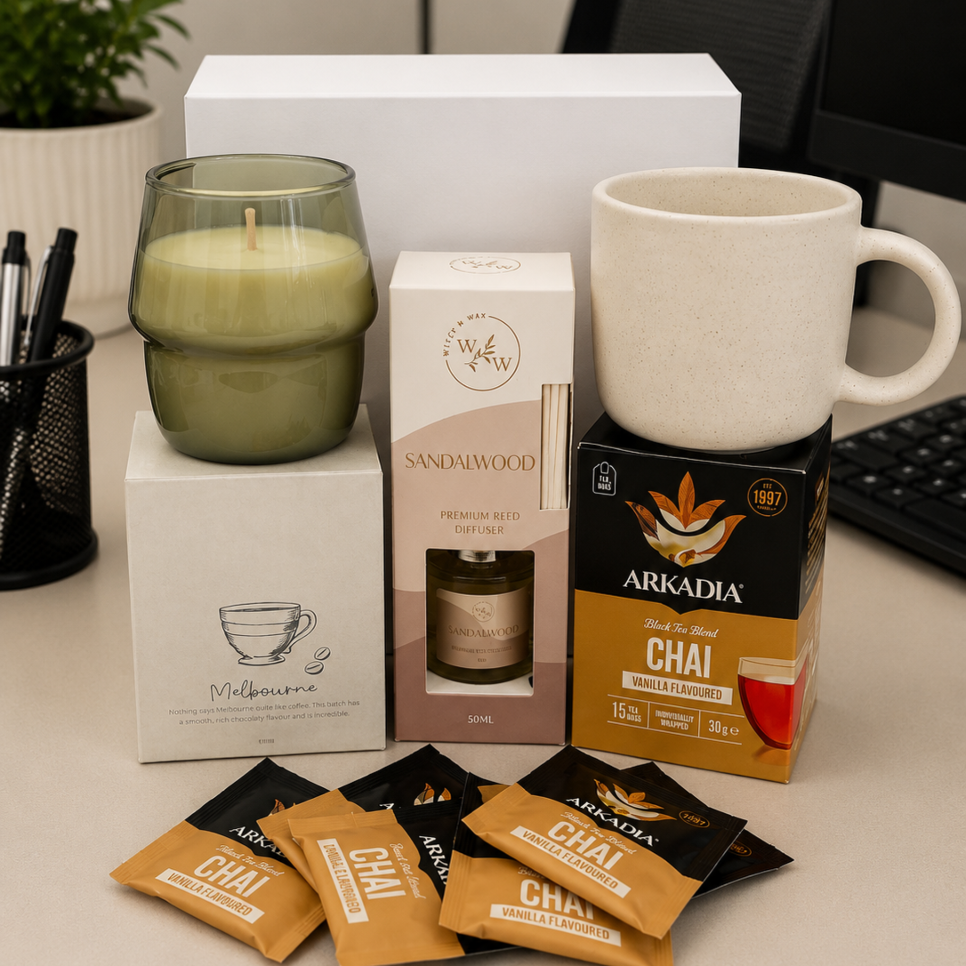 Arkadia Chai tea packaging with a candle, box, and mug on a desk.