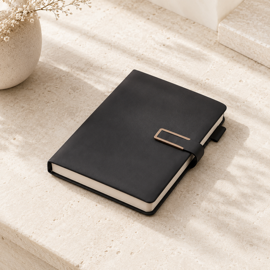 Black notebook with a gold buckle on a light stone surface