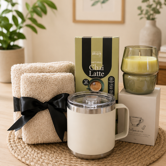 Gift set with towels, mug, and tea box on a wooden surface with plants in the background
