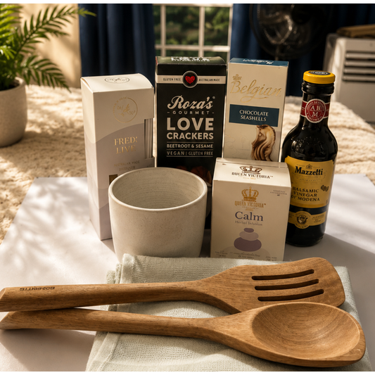 Table with wooden utensils, boxes of snacks, and a bottle of olive oil.