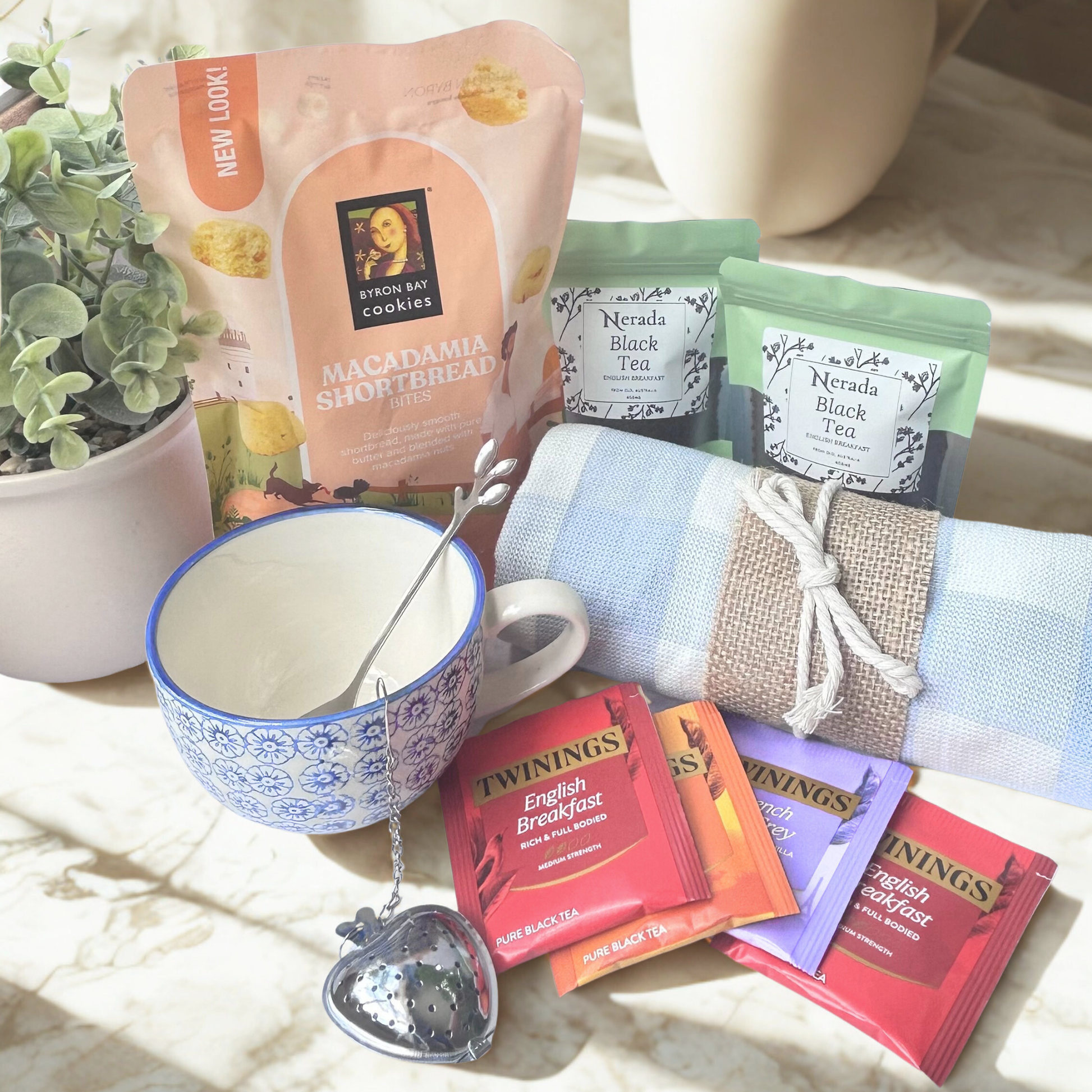 Tea packaging including Twinings English Breakfast tea bags, a mug with a tea infuser, and cookies on a light background.