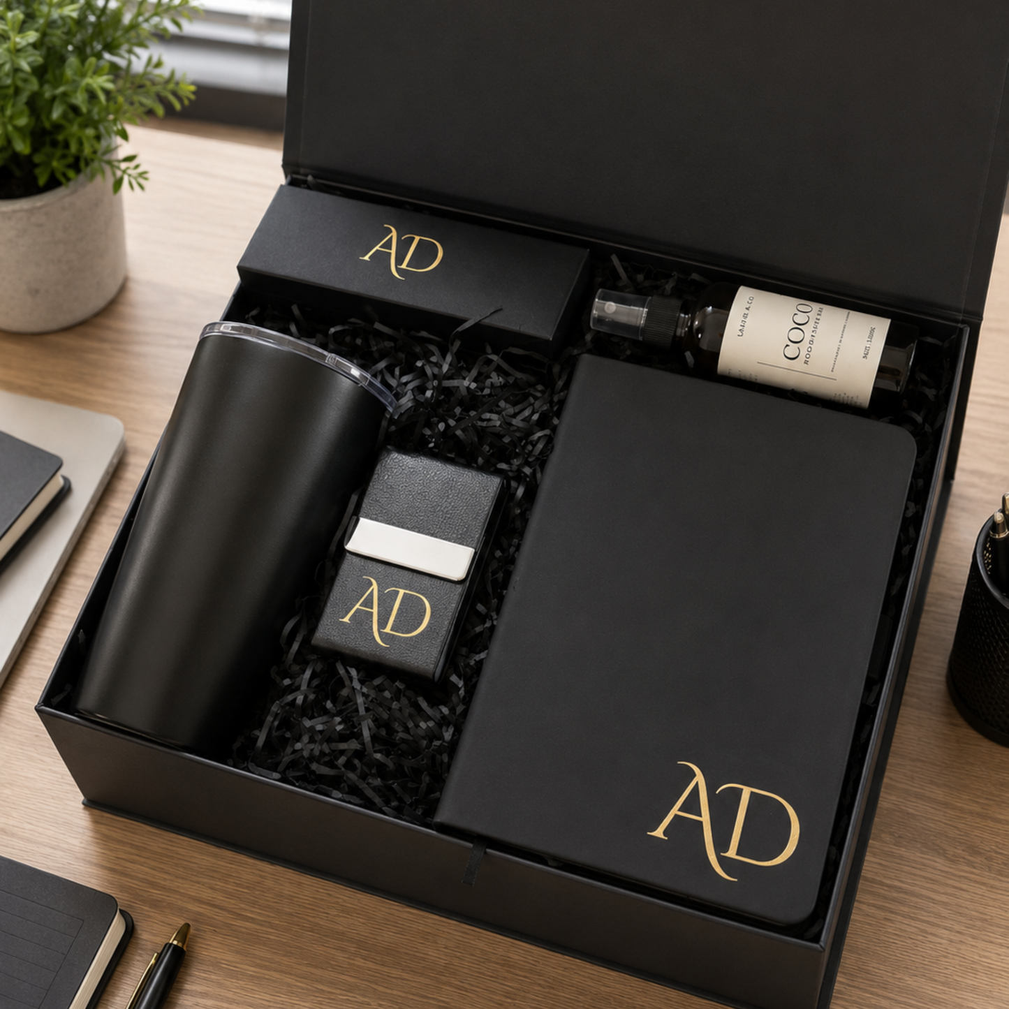 Gift set with black tumbler, notebook, and small bottle in a black box with 'AD' logo.